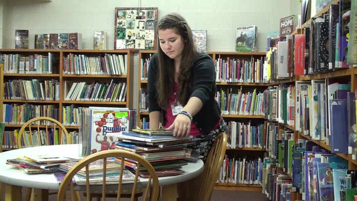 Person in Library picking up a book from a stack of books